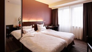 Quarto de hotel com uma cama grande, uma mesa, uma cadeira, um espelho e uma janela com cortinas.