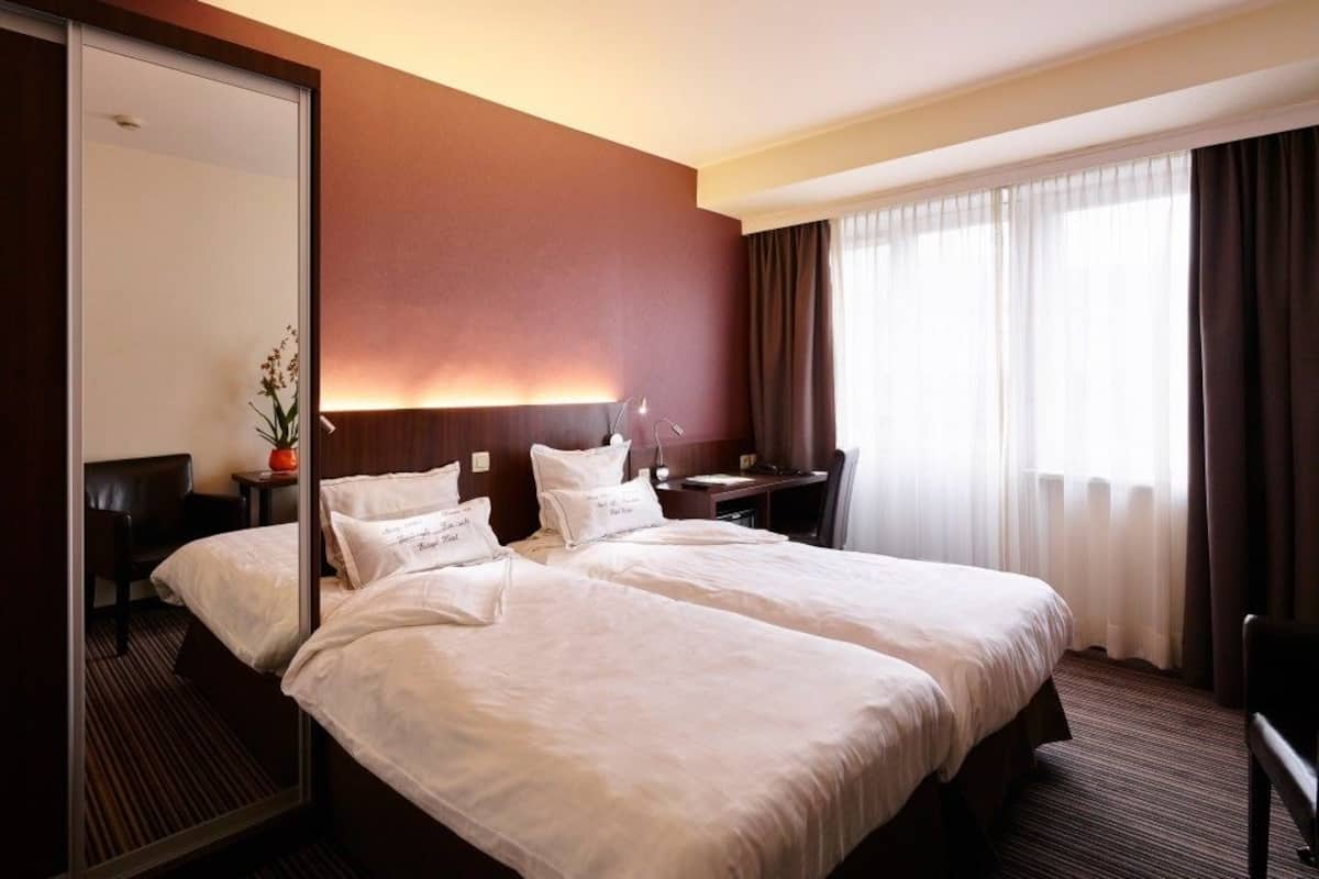 Habitación de hotel con una cama grande, un escritorio, una silla, un espejo y una ventana con cortinas.