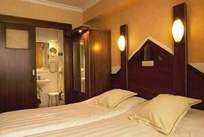 A hotel room with a bed, two bedside lamps, a wooden headboard, and a bathroom visible through an open door.