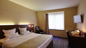Een hotelkamer met een groot bed, een bureau met lamp, een stoel, een televisie en een raam met gordijnen.