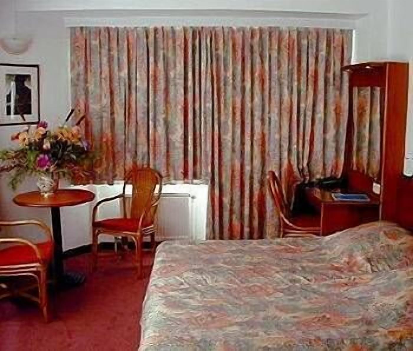 Une chambre d’hôtel avec un lit, un bureau, une chaise et un radiateur.