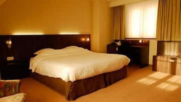 A hotel room with a large bed, a desk, a chair, and a wardrobe.