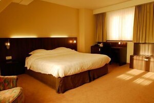 A hotel room with a large bed, a desk, a chair, and a wardrobe.