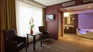 Quarto de hotel com área de estar, televisão e banheiro com banheira e pia.