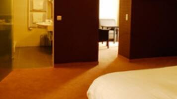 Una habitación de hotel con una cama grande, un televisor en la pared y un baño visible a través de una puerta abierta.