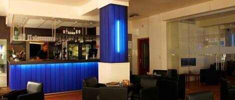 Zona de bar con una pared azul decorativa, asientos con sillas negras y un cantinero.