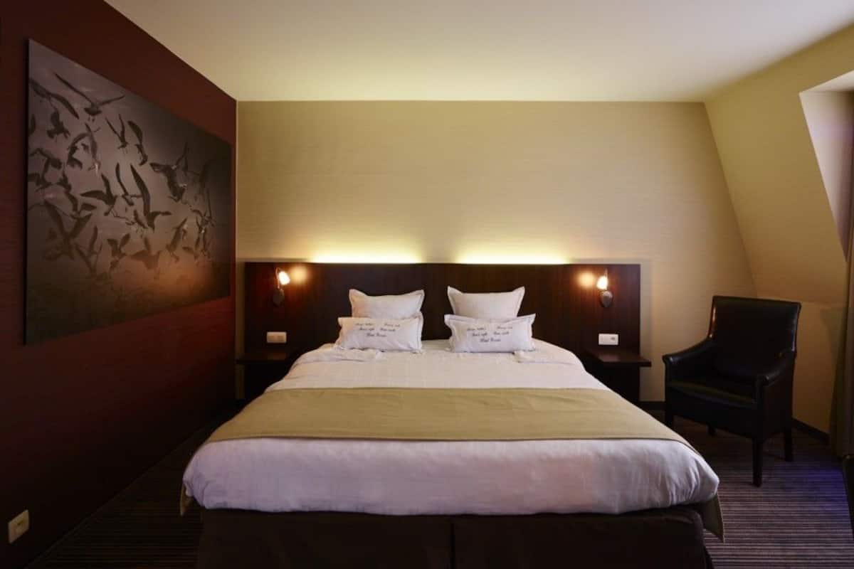 Una habitación de hotel con una cama grande, dos mesitas de noche, una silla y una obra de arte colgada en la pared.