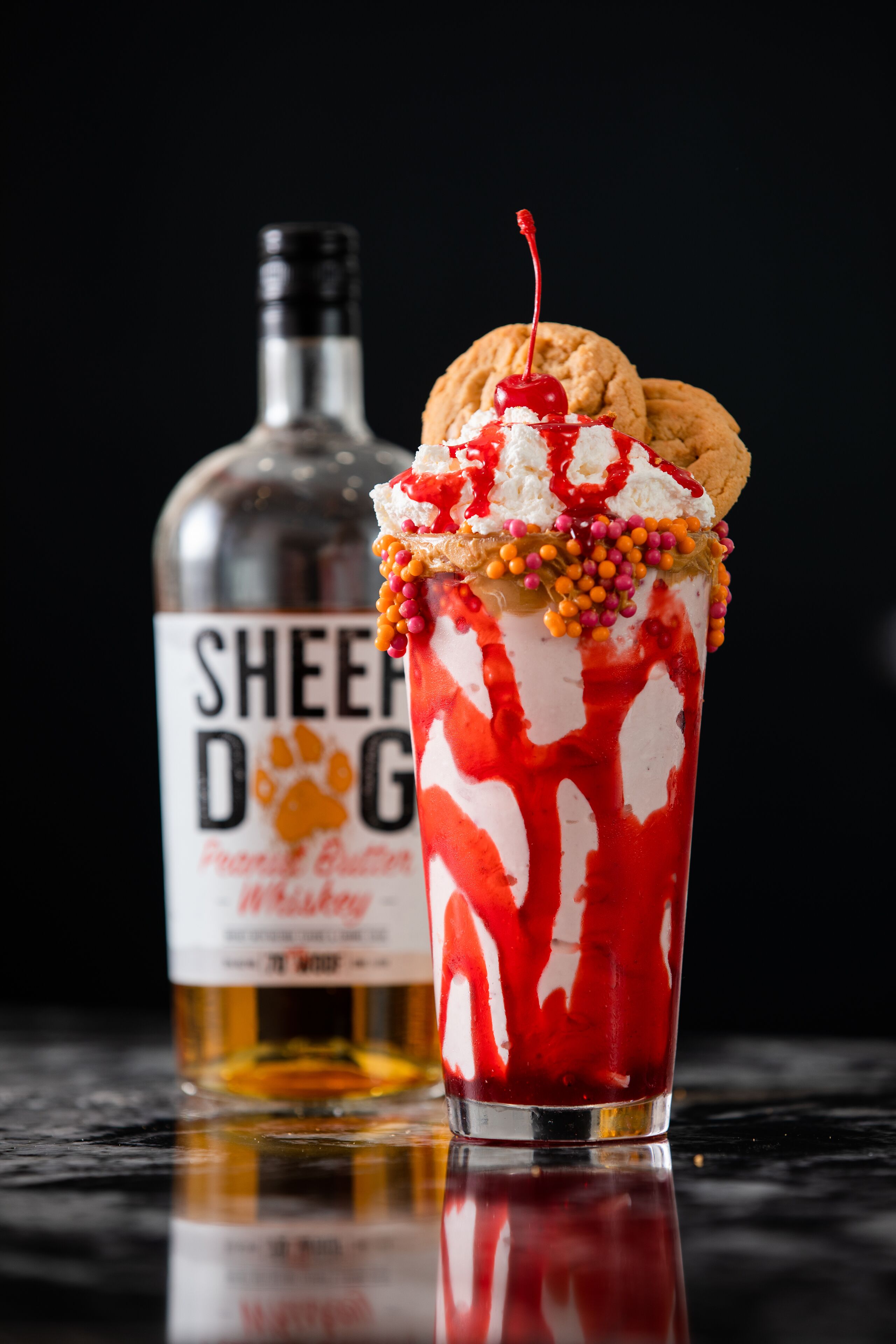 A dessert drink with a cookie and a cherry on top, and a bottle labeled "Sheep Dog" in the background.