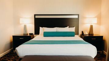 Een hotelkamer met een groot bed, twee nachtkastjes, een bankje en een hoofdbord.