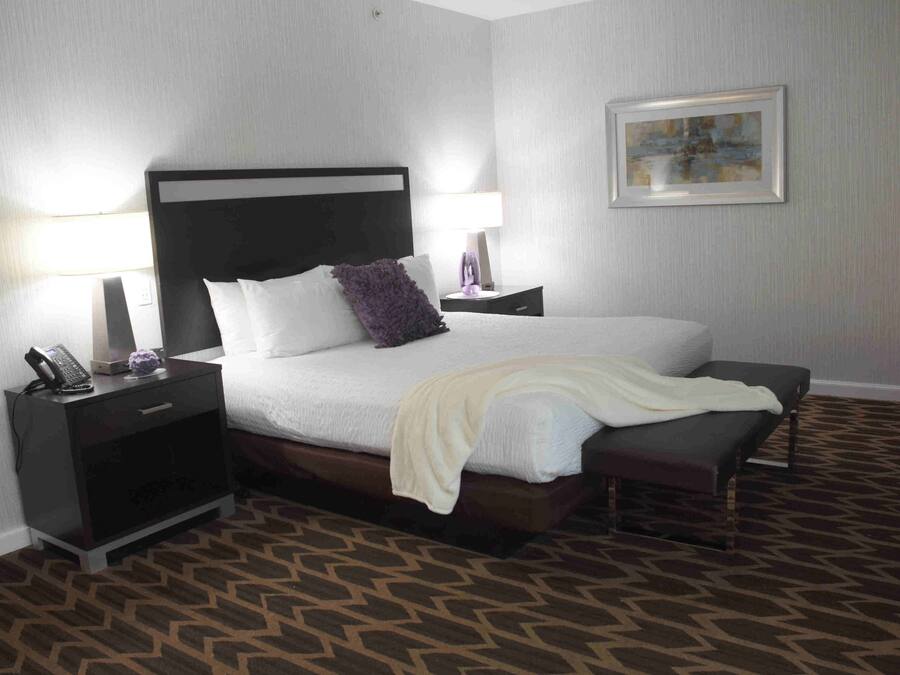 A hotel room with a large bed, two bedside tables, a nightstand, a bench, a lamp, and a framed picture on the wall.