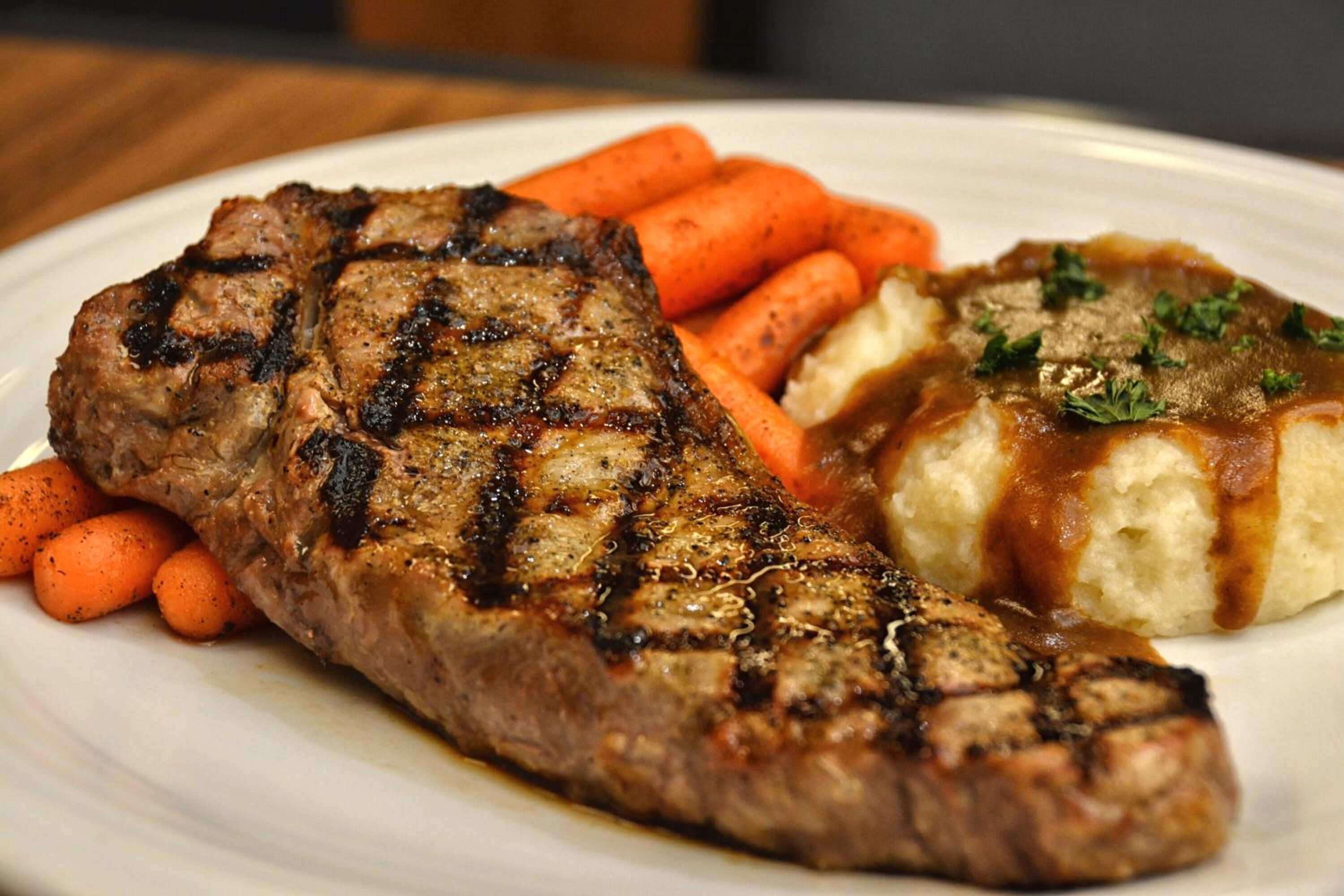 A steak with grill marks, carrots, and mashed potatoes with gravy on a plate.