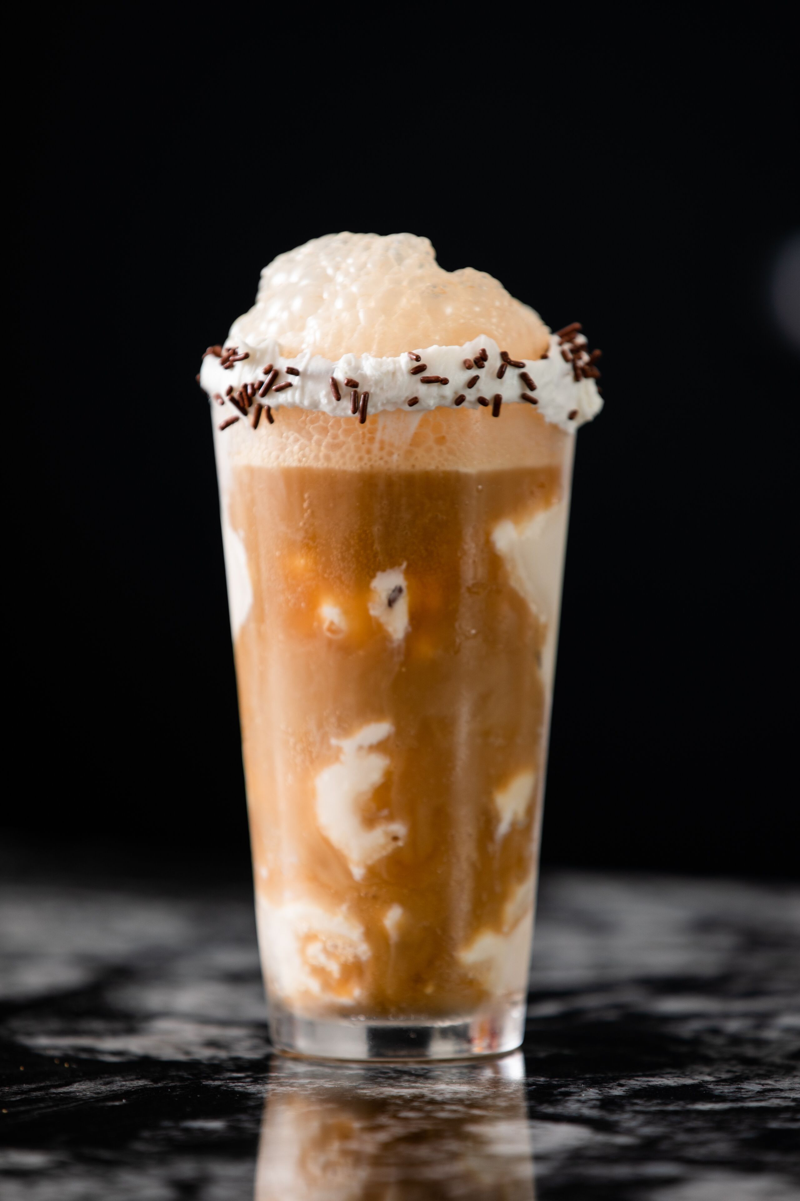 Un grand verre de café glacé, surmonté de crème fouettée et de vermicelles au chocolat.