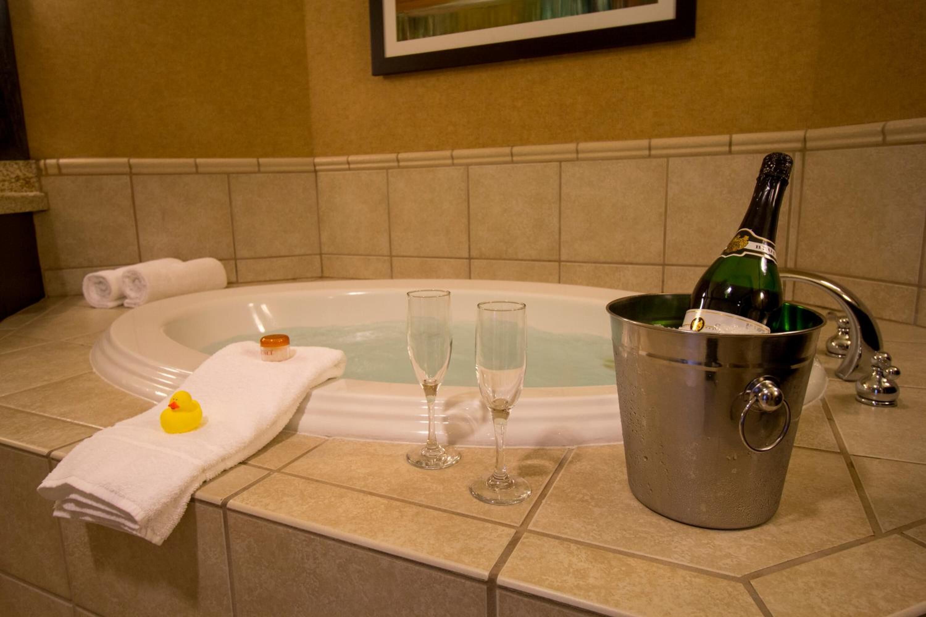 A bathroom with a bathtub, two champagne flutes, a rubber duck, and a bottle of champagne in a bucket.