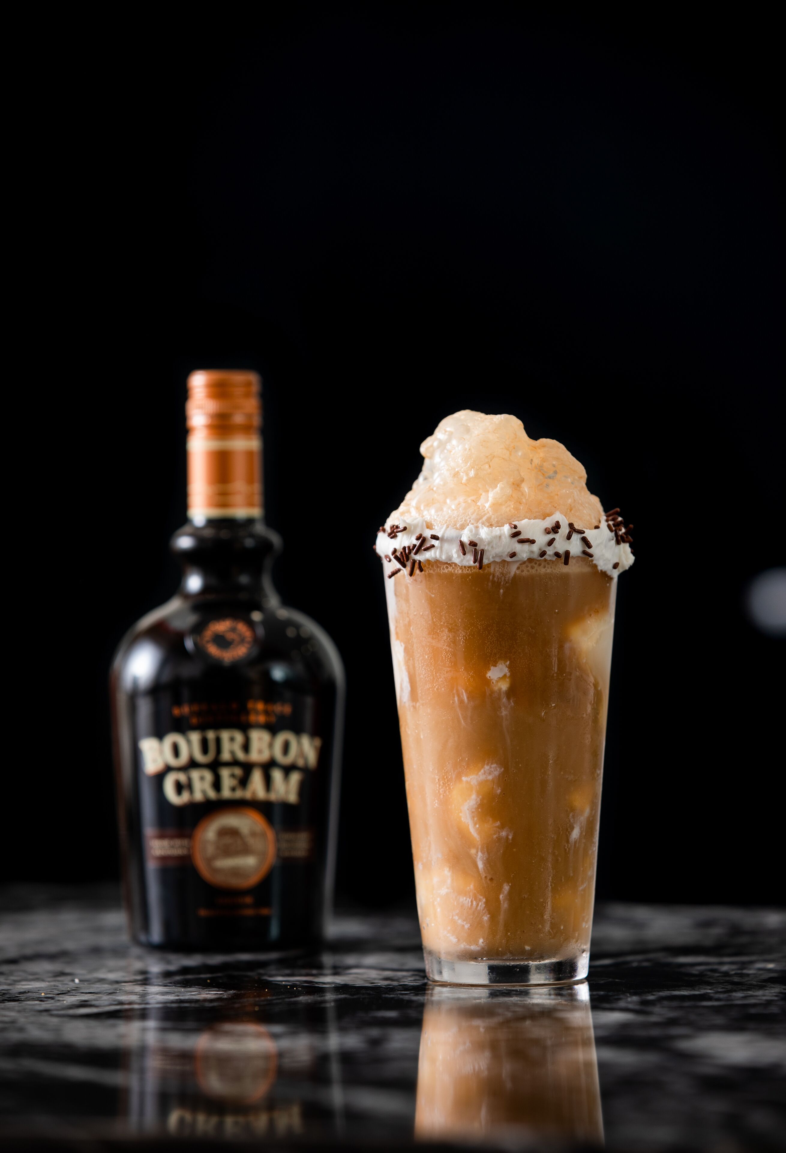 Een fles bourbonroom en een glas met een romige drank en ijs.