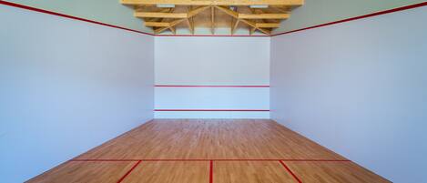 Una cancha de squash con piso de madera y líneas delimitadoras rojas.
