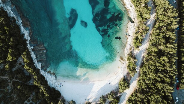Luchtbeeld van een kustgebied met helder turquoise water, een zandstrand en weelderige begroeiing.
