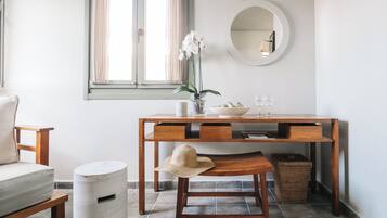 A room with a wooden desk, a chair, a small round table, a trash bin, a wicker basket, and a potted orchid.