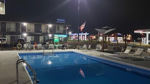 A nighttime pool area with lounge chairs, a pool, and a building with a 'Welcome' sign. - Niagara Falls Courtside Inn (Niagara Falls)