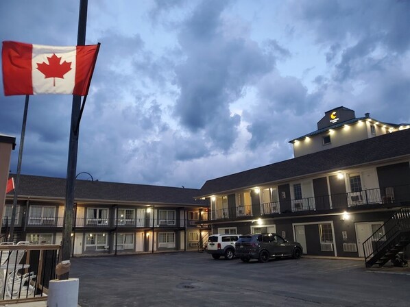 A motel with multiple floors, outdoor parking, and a Canadian flag. - Niagara Falls Courtside Inn (Niagara Falls)