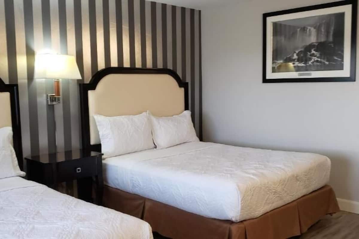 A hotel room with two beds, a striped wall, a framed picture, and a nightstand with a lamp.