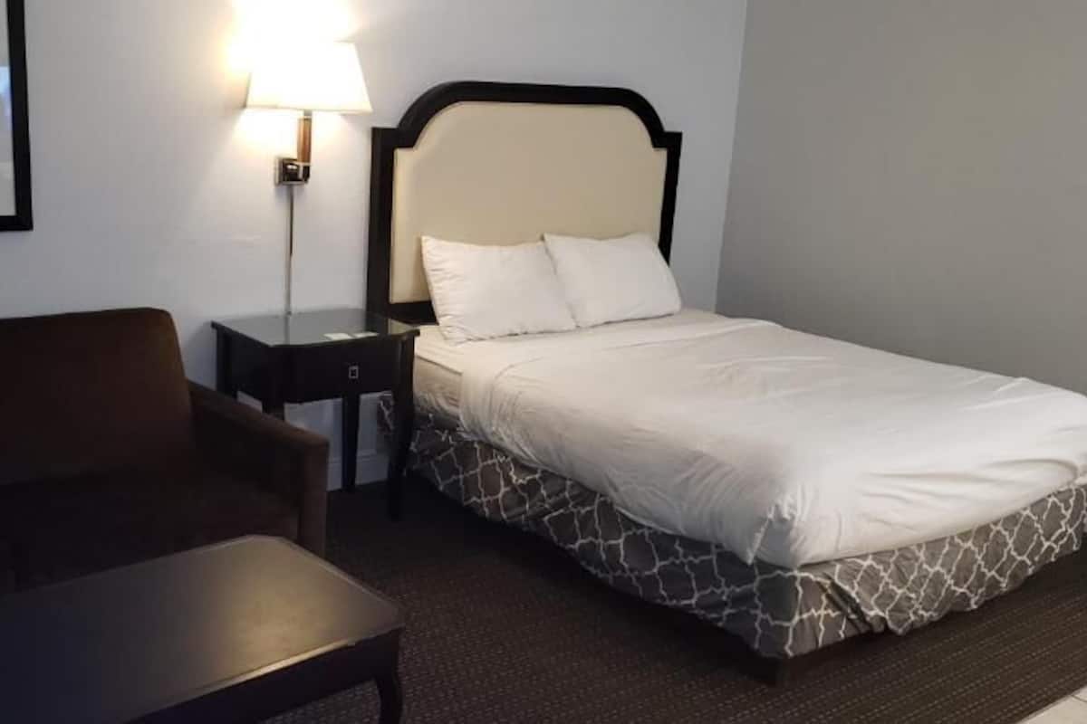 A hotel room with a bed, a nightstand, a lamp, a framed picture on the wall, and a sofa.