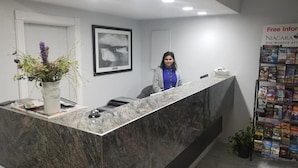 A reception desk with a marble top, a framed picture on the wall, a potted plant, and a magazine rack. - Niagara Falls Courtside Inn (Niagara Falls)
