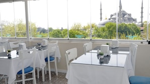 A dining area with white tables and chairs, large windows offering a view of a mosque with domes and minarets.