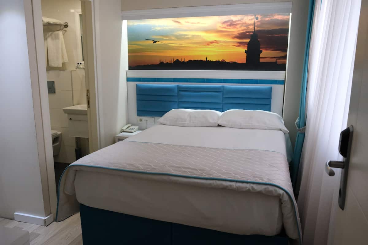Une chambre avec un lit, une vue sur un coucher de soleil et une salle de bain visible à travers une porte ouverte.