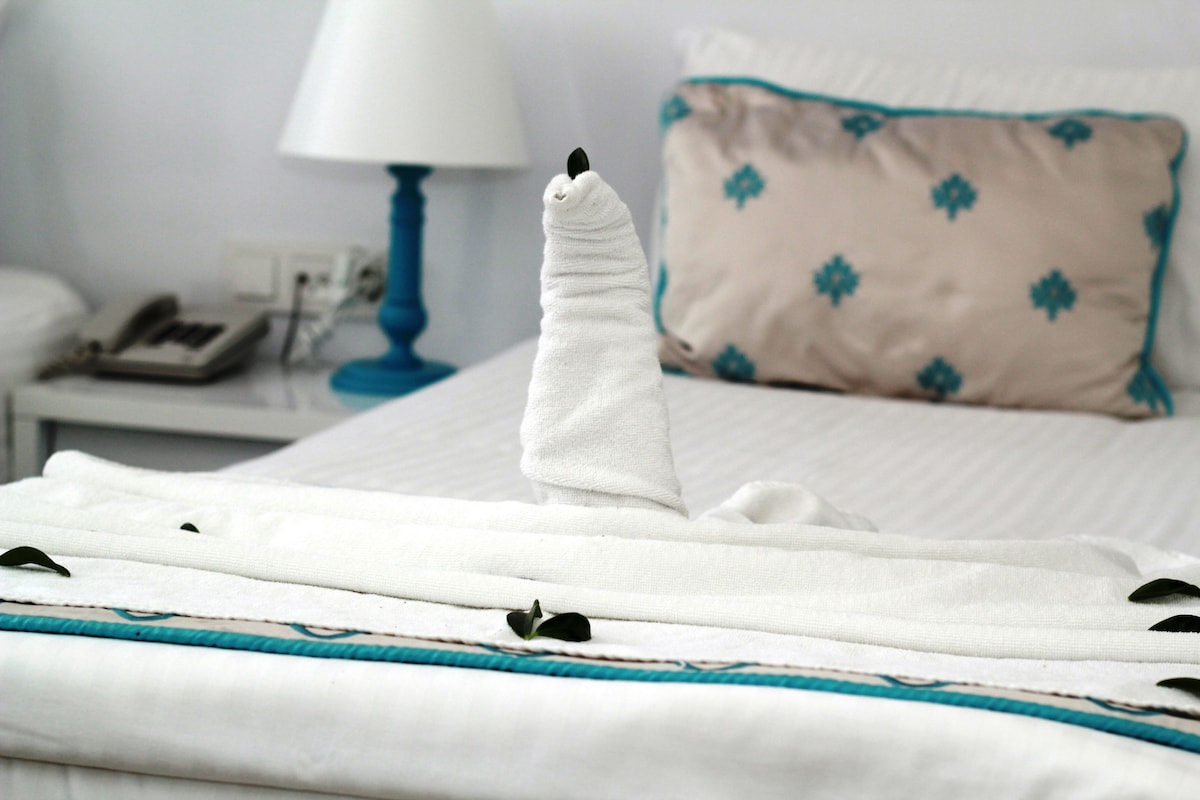 Una cama bien hecha con una manta blanca y una almohada decorativa.