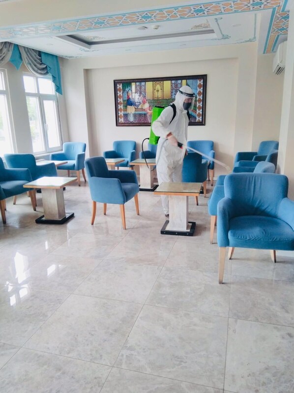 Un vestíbulo de hotel con sillones azules, un cuadro grande en la pared y una persona con traje protector blanco.