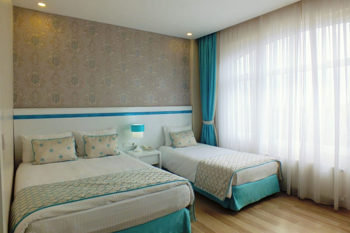 Une chambre d’hôtel avec deux lits, une table de chevet, une lampe et une fenêtre avec des rideaux.