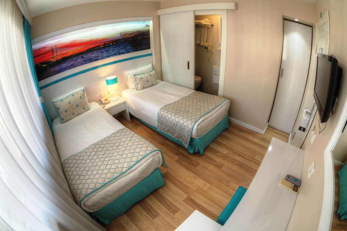 Une chambre d’hôtel avec deux lits, une télévision, un bureau et une salle de bain visible à travers une porte ouverte.