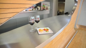 A modern bar area with a wooden panel design, two glasses of red wine, and a small plate of appetizers. - Hotel Zone (Rome)