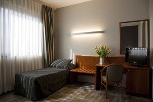 Camera d'albergo con un letto, una scrivania con una sedia, una televisione e un vaso con fiori.