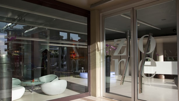 A modern interior with a glass door, a white sofa, and a small table. - Hotel Zone (Rome)