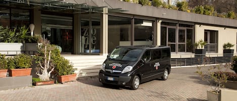 A modern building with a paved entrance, a parked van, and potted plants.