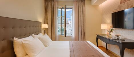 Quarto de hotel com uma cama grande, uma escrivaninha e uma televisão na parede.