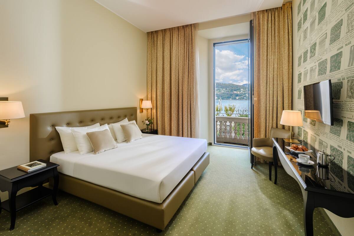 Une chambre d’hôtel avec un grand lit, un bureau avec une chaise, une télévision et un balcon donnant sur l’eau.