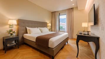 Habitación de hotel con una cama grande, dos mesitas de noche, un televisor de pantalla plana y vista a la ciudad.