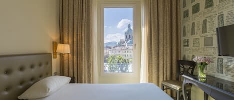 Habitación de hotel con cama, escritorio, lámpara y vista a un edificio a través de una ventana.