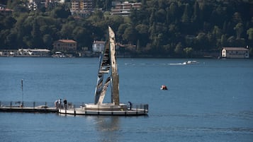 Una escultura frente al agua con una superficie reflectante, rodeada por un muelle y algunas personas.