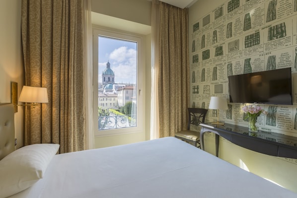 A hotel room with a bed, a desk with a TV, a window with curtains, and a wall with printed text.