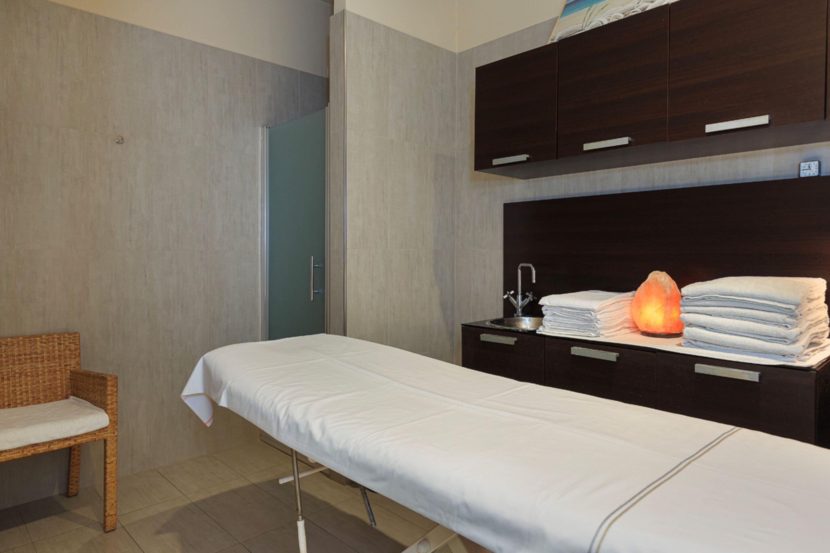 A hotel room with a bed, a bedside table with a lamp, a chair, and a wardrobe.