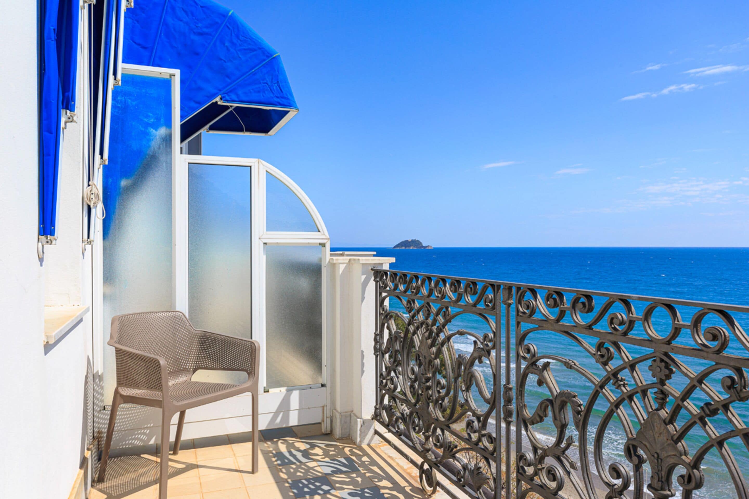 A balcony with a metal railing, a chair, and a blue umbrella.