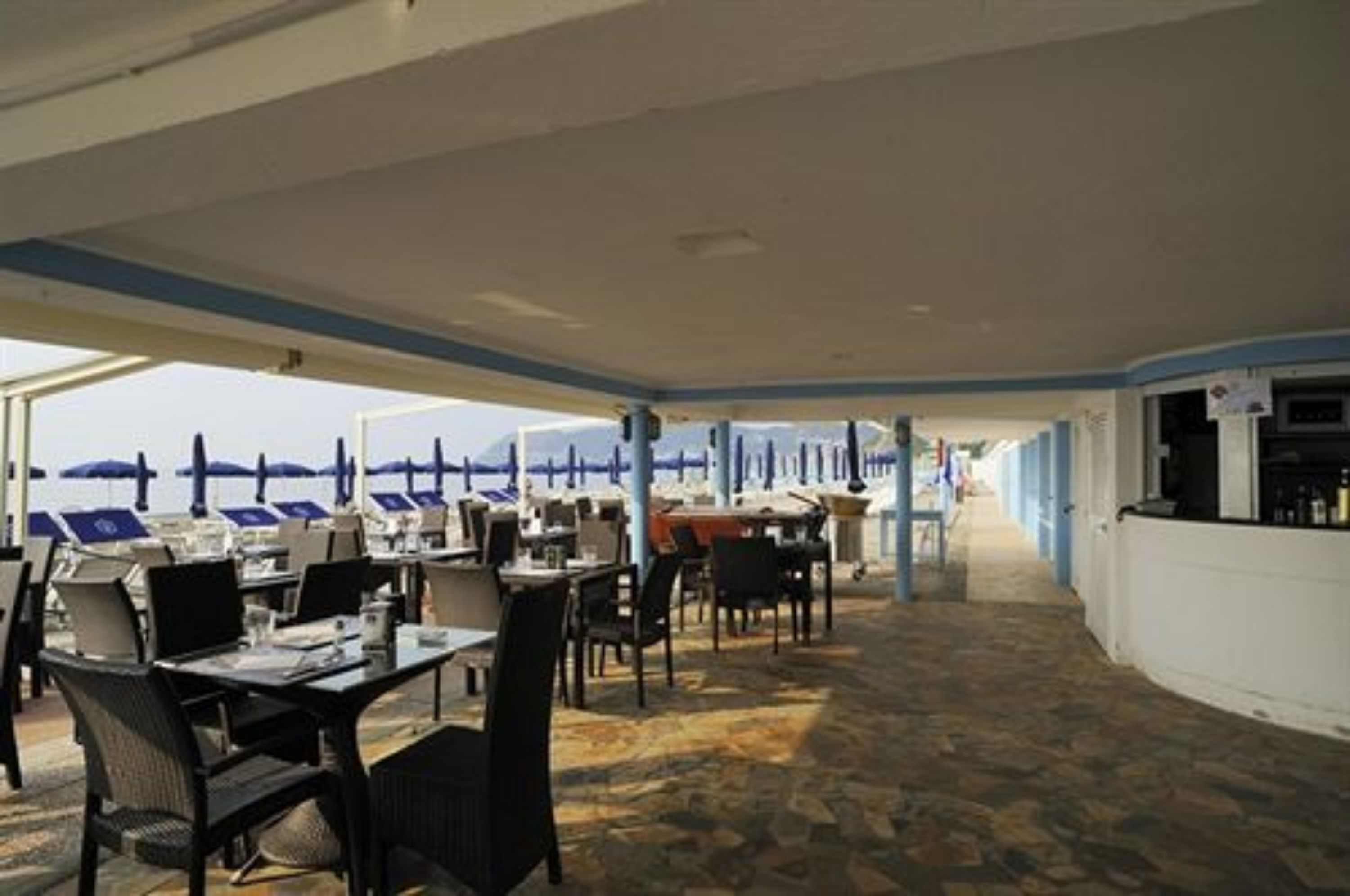 Un área de comedor al aire libre con mesas, sillas, sombrillas y vistas al mar.