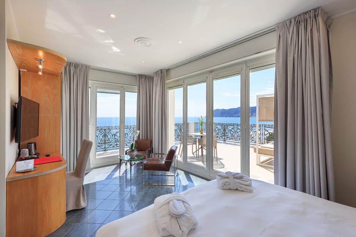 Ein Hotelzimmer mit einem großen Bett, einem Schreibtisch und einem Balkon mit Meerblick.