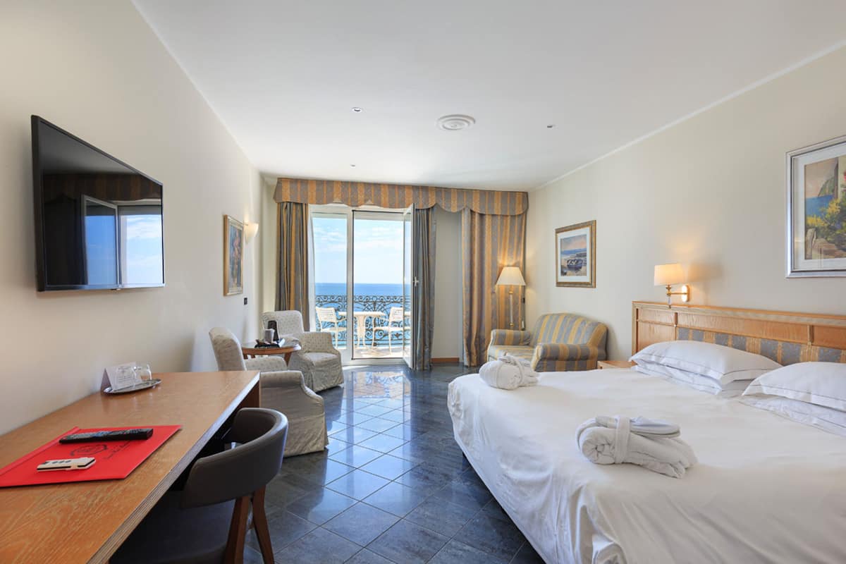 Ein Hotelzimmer mit Bett, Schreibtisch, Stuhl, Fernseher und einem Balkon mit Blick.
