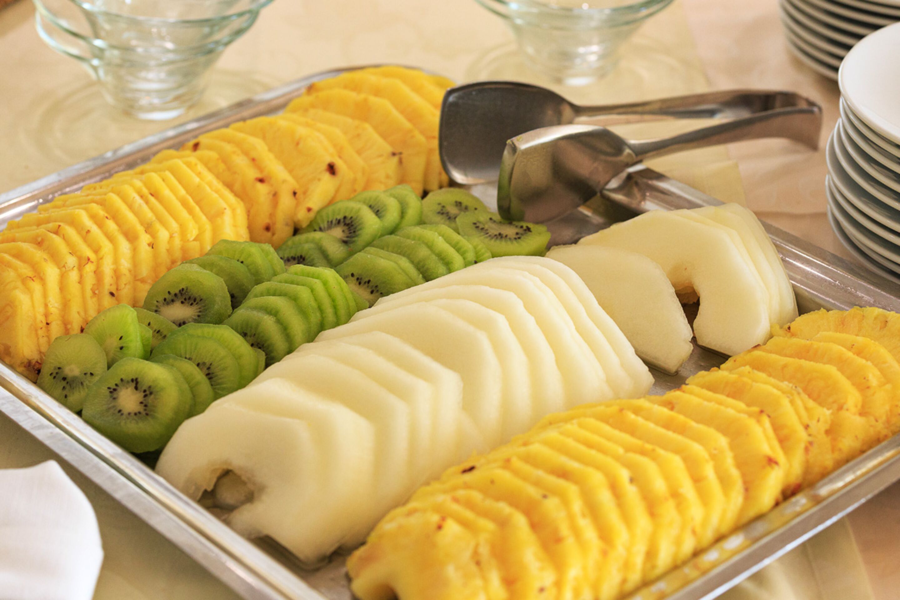 Une assiette de fruits coupés en tranches, notamment du kiwi, de l’ananas et de la mangue, disposés sur un plateau de service en métal.