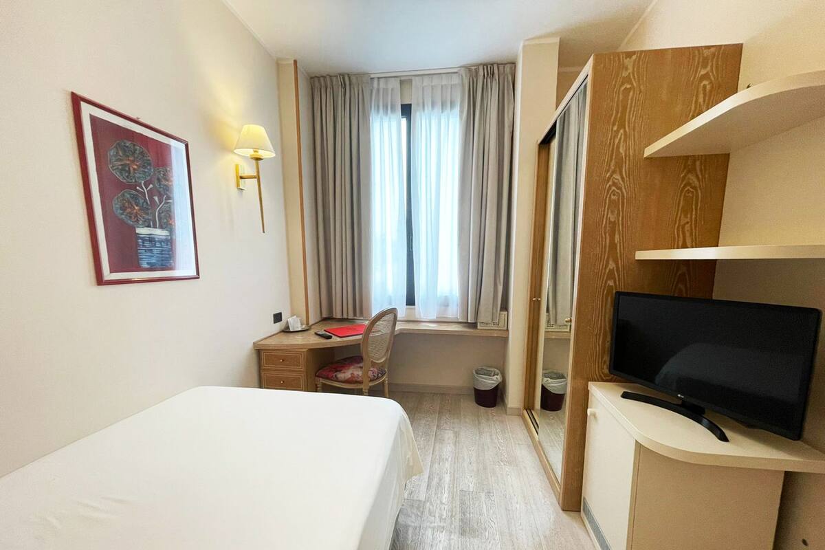 Ein Hotelzimmer mit Bett, Schreibtisch mit Stuhl, Fernseher und einem Fenster mit Vorhängen.