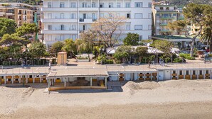 Un hotel de varios pisos con balcones, situado cerca de una playa con arena y un estacionamiento.